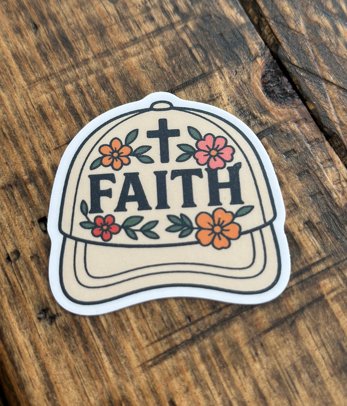 Sticker of a cap with 'FAITH' text and floral designs on a wooden surface